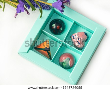 Tempered chocolate candies with glossy painted body in a box with blur elements. View from above. Stock photography.