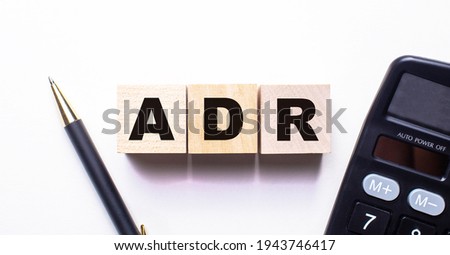 The words ADR Alternative Dispute Resolution is written on wooden cubes between a pen and a calculator on a light background.