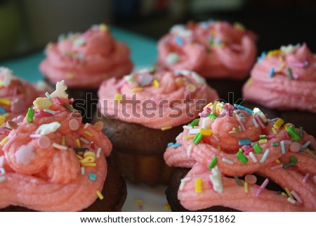 A small shaped cupcake with pink cream and sprinkles on a white plate. Blue background.