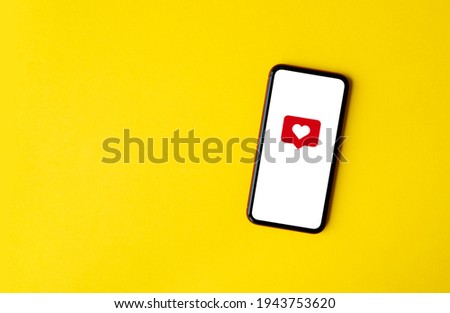 Top view of cell phone with heart emoticon. White screen and yellow background, copy space. Social network concept.