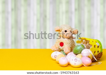 Easter greeting card template. Decorative composition of colorful eggs with a easter lamb and eggs on a yellow table in front of modern abstract curtain background. Copy space. Religion and culture co