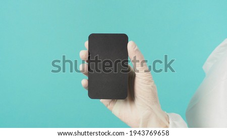 Hand holding empty blank black card.Hand with ppe suit, latex glove on green or Tiffany Blue background. Empty space for text