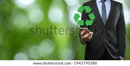 Businessman in suit over natural green background holds an recycling icon, sign in his hands. Ecology, environment and conservation concept.