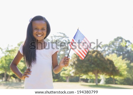 Little girl smiling at camera waving american flag on a sunny day
