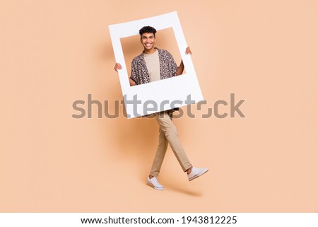 Full length portrait of cheerful dark skin guy hands hold paper frame beaming smile isolated on beige color background