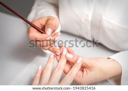 French manicure. Manicure master drawing white varnish on the nail tip with a thin brush, close up Royalty-Free Stock Photo #1943825416