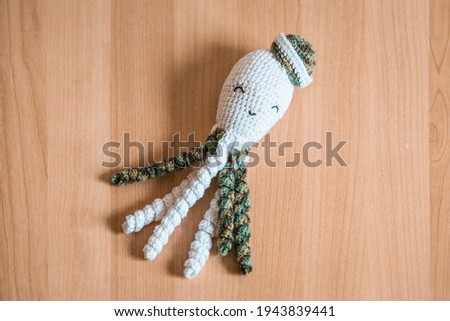 A squid or octopus soft plush toy for a child or infant, made from crochet yarn. Pictured on a light wooden surface