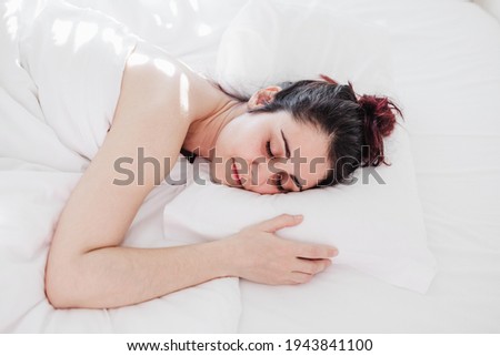 Top view of attractive young woman sleeping well in bed hugging soft white pillow. girl resting, good night sleep concept. Lady enjoys fresh soft bedding linen and mattress in bedroom