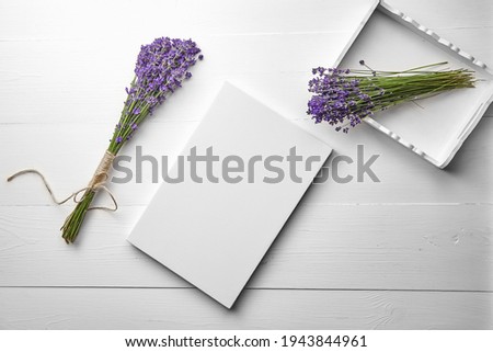 White canvas mockup and lavender flowers bouquet in tray on white wooden table background, flat lay. Blank canvas, top view