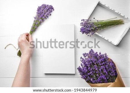 White canvas mockup and hand with lavender flower bouquet on white wooden table background, flat lay. Blank canvas, top view