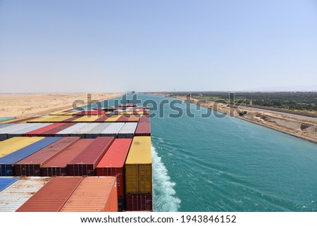 View on the containers loaded on deck of cargo ship. Vessel is transiting Suez Canal on her international trade route. Suez canal landscape. Royalty-Free Stock Photo #1943846152
