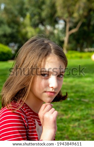 portrait of a thoughtful cute happy beautiful natural teenage girl in a red striped t-shirt against the greenery on a sunny day