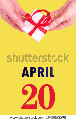April 20th. Festive Vertical Calendar With Hands Holding White Gift Box With Red Ribbon And Calendar Date 20 April On Illuminating Yellow Background. Spring month, day of the year concept.