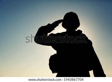 Silhouette of soldier in combat helmet and ammunition saluting on background of sunset sky. Army special forces fighter, Marines rifleman showing respect, greeting officer with salute gesture Royalty-Free Stock Photo #1943867704