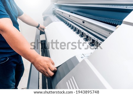 man holding printable material on alarge format printing plotter.graphic design and advertising concept.