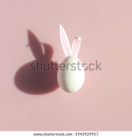 Easter egg with bunny ears and shadow on pastel pink background. Creative easter concept.
