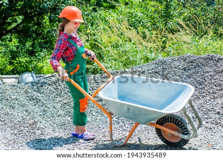 cheerful child laborer using building uniform and construction wheelbarrow, future career