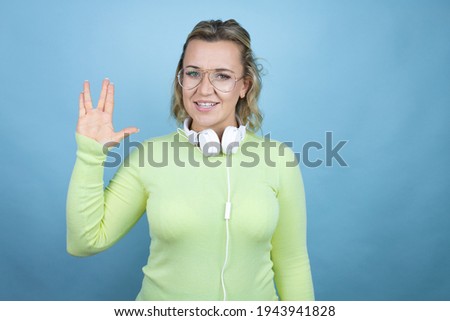 Young caucasian woman wearing headphones on neck over blue background doing hand symbol