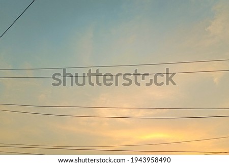 Silhouette electric lines on yellow sky background. Electric wires on cloudy sky background. Beautiful tiny and soft clouds at sunset. Unorganised wires. Nature photography. Sky picture in sunlight