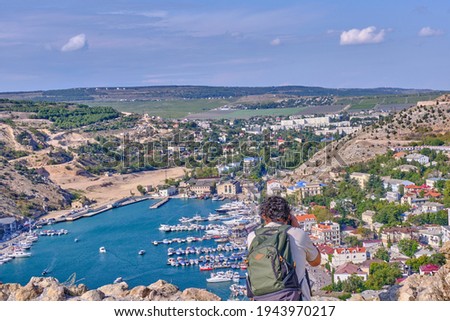 Top view of the Balaklava Bay, city Sevastopol, Crimean Peninsula, Russia. A male tourist with a backpack takes photos with a camera