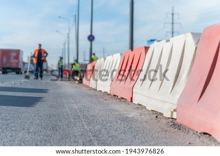 Red and white plastic safety barriers along the road and blurred workers in the background
