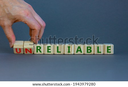 Unreliable or reliable symbol. Businessman turns wooden cubes and changes the word unreliable to reliable. Beautiful grey background, copy space. Business and unreliable or reliable concept. Royalty-Free Stock Photo #1943979280
