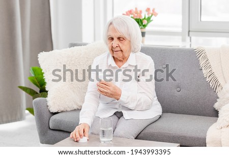 Eldery woman sitting on the sofa and looking at packaging of pills at home