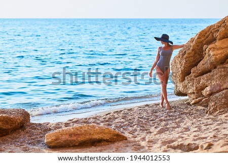 Young woman in swimsuit posing on seashore near rock. Summer lifestyle and summertime idea. Seascape on background.