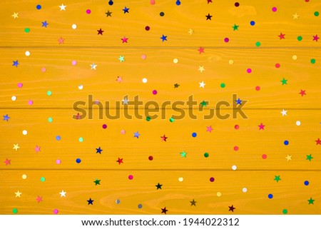 Above photo of multicolored rainbow confetti isolated on the yellow wooden background with empty space