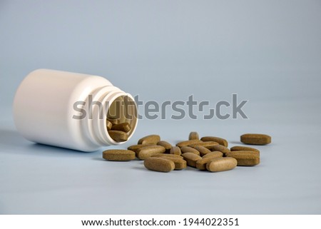 Natural brown pressed medicinal herb,pills in open upturned plastic jar on table front. Alternative medicine concept of drugs, tablets, medicines and pills on gray background. Copy space. Royalty-Free Stock Photo #1944022351