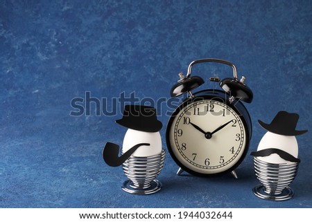 Easter creative holiday concept. White eggs of a chicken farm on a blue background. Gentlemen at breakfast. Alarm clock and time. Copy space.