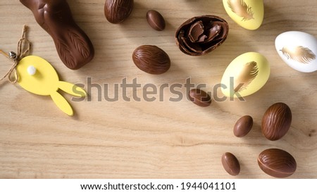 Easter Decor, Pastel Yellow and Chocolate Eggs, rabbit and cakes  on wooden background.  Top view. Banner format
