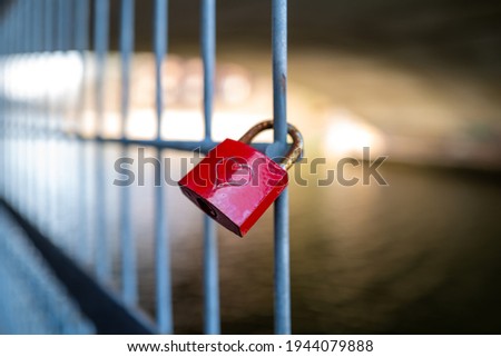 a red padlock on which is engraved a heart hangs on a fence