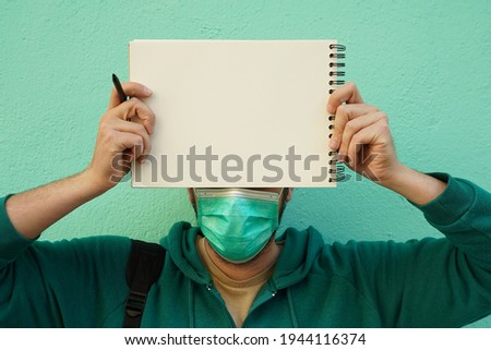 A young Hispanic male from Spain with a face mask holding a blank paper with space for text - conveying an important message