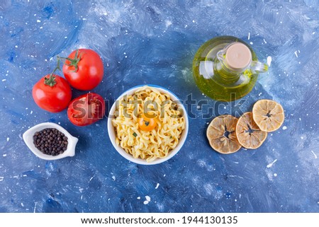 Homemade noodles with fried chicken wing, tomatoes, olive oil, seared lemon slices, black pepper on galaxy blue background. High quality photo