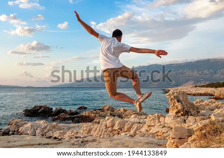 A young Caucasian male posing for a picture by jumping on the rocks at the beach