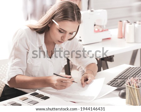 Long hair beautiful young fashion designer working on pattern sketching and fabric samples in the studio. Professional dressmaker design stylish women clothing. Female fashion factory business concept