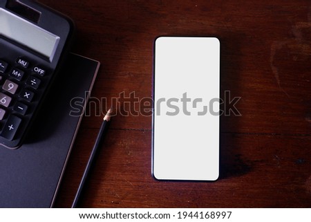 Cropped shot view of wood office desk table with smart phone with white blank screen in modern place.