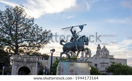  View of Balboa Park's El Cid Campeador statue, and the House of Charm building on the background with beautiful sunset sky.