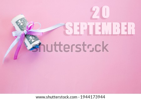 calendar date on pink background with rolled up dollar bills pinned by pink and blue ribbon with copy space. September 20 is the twentieth day of the month.