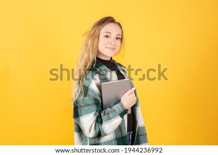 pretty blonde woman in casual clothes, with a tablet, on yellow background
