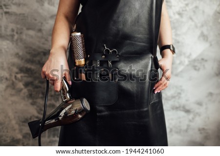 Person in black apron with professional hairdresser set on dark background, closeup Royalty-Free Stock Photo #1944241060