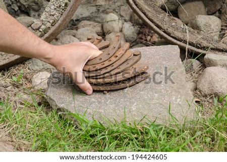 man hand put old rusty iron horseshoe pile on stone outdoor 