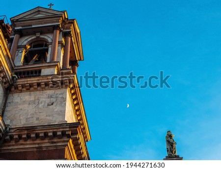 Facade of St. Isaac's Cathedral in St. Petersburg with a tower and a cross against the background of a blue sky and a growing moon on the side of the southern entrance. View from the west side of the 