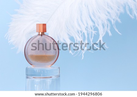 Unbranded round perfume bottle on glass podium and large white ostrich feather on blue background. Transparent glass perfume bottle for branding and label. Eau de toilette. Mockup