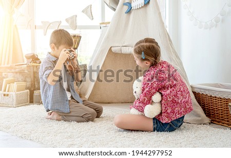 Little boy taking pictures of little girl with retro camera in children's room
