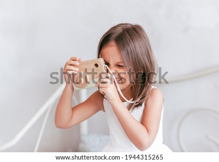 A little girl plays with a toy camera. Takes a picture of a child
