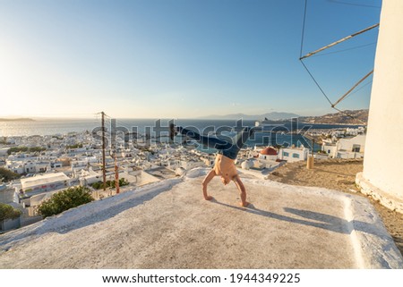 Tourist doing handstand in front of Mykonos skyline, Cyclades, Greece