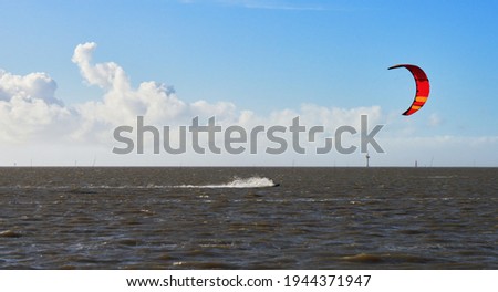 kite surfer with colorful red sail at the North Sea coast in Wremen (Germany) in high speed in front of blue sky with white clouds