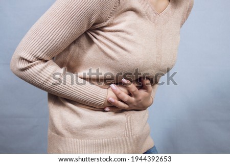 girl holding her stomach in pain on a gray background